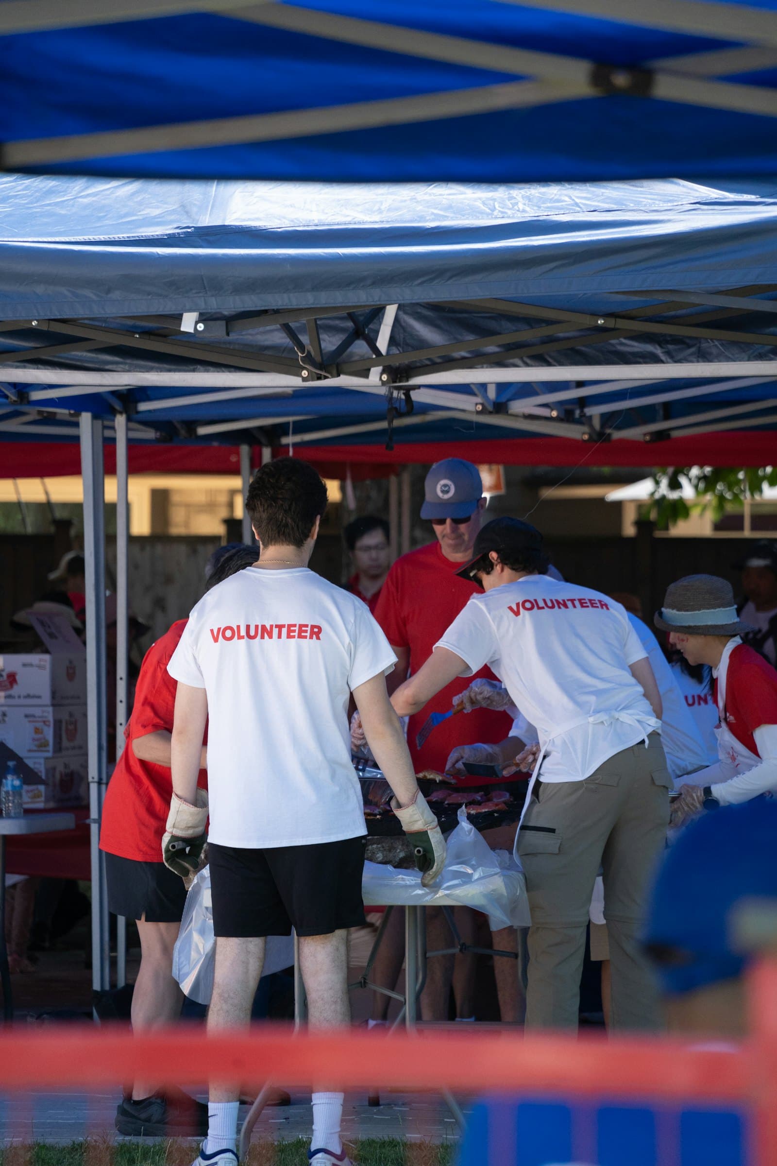 Volunteers organizing supplies under a blue tent at an outdoor event.