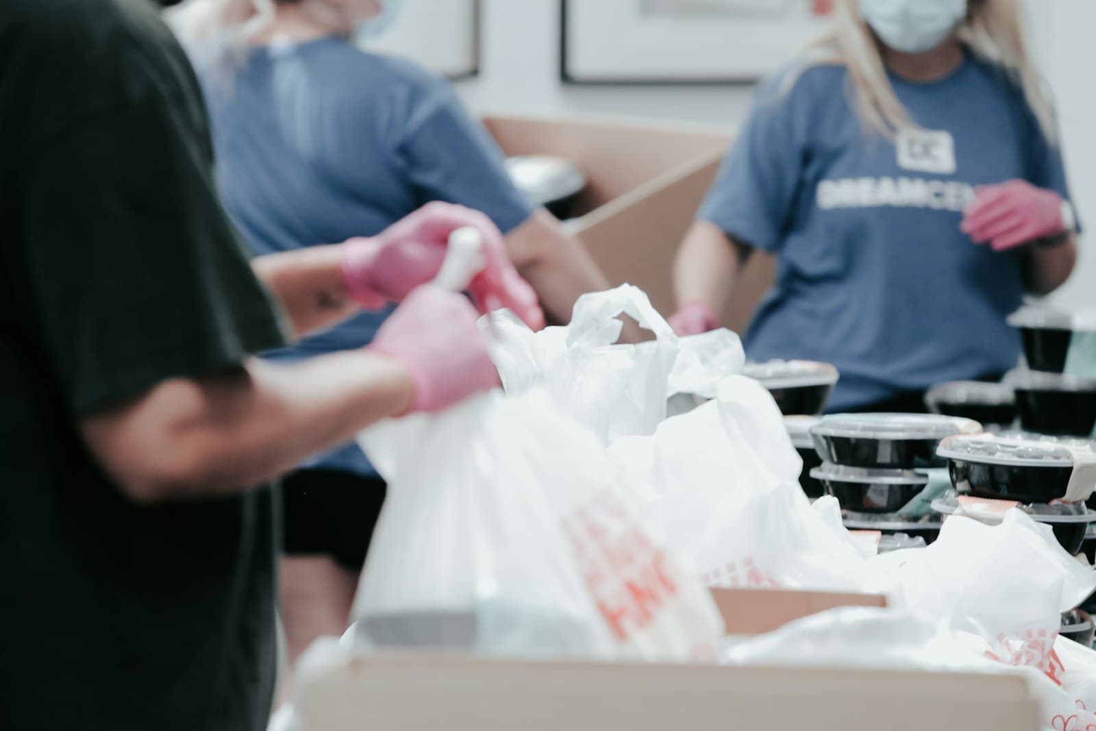 Volunteers in blue shirts and pink gloves packing food into bags.