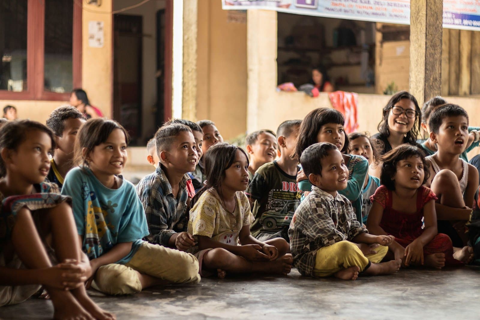 Children sitting together on the floor of a bright community hall, listening during a group session.