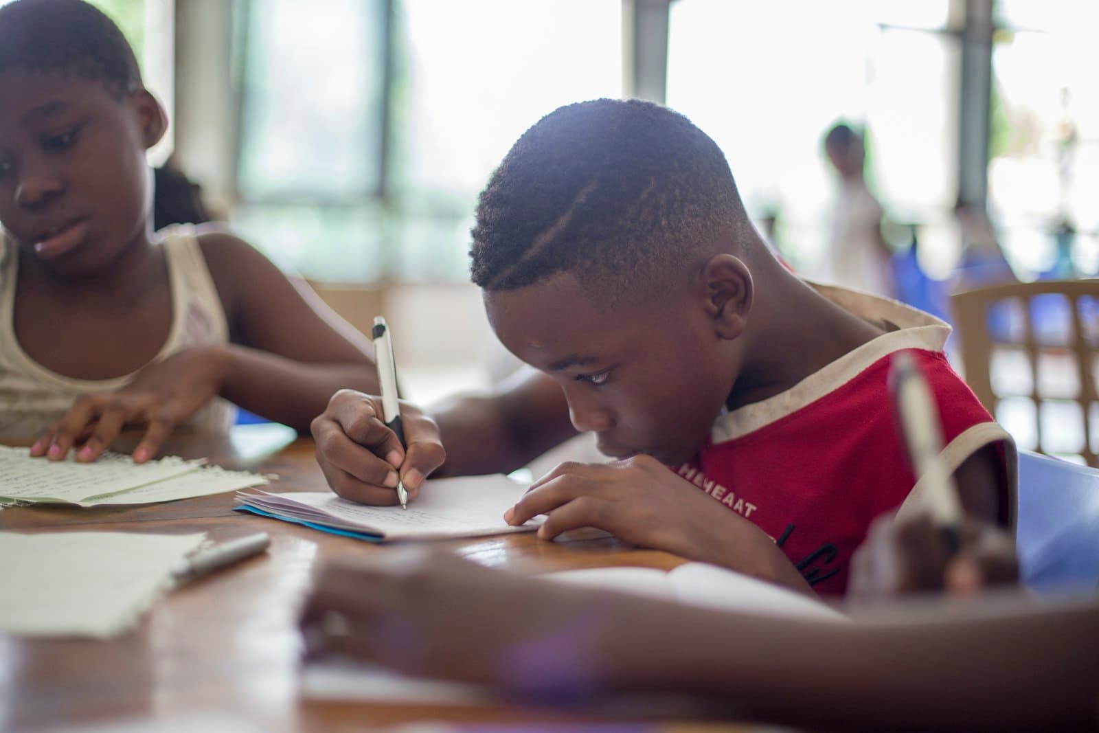 Two students concentrating as they write in their notebooks at a shared desk.