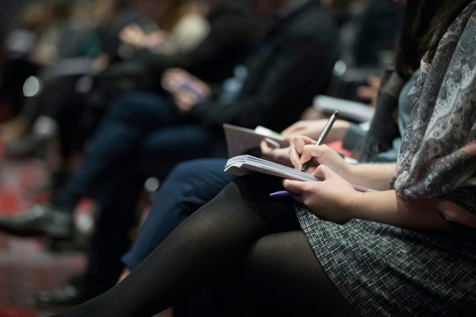 People seated in rows taking notes in their notebooks during a meeting.
