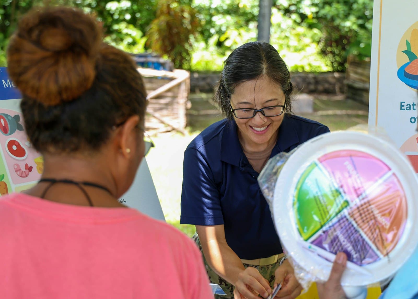 A health educator showing a woman a plate divided into food groups at an outdoor information stand.
