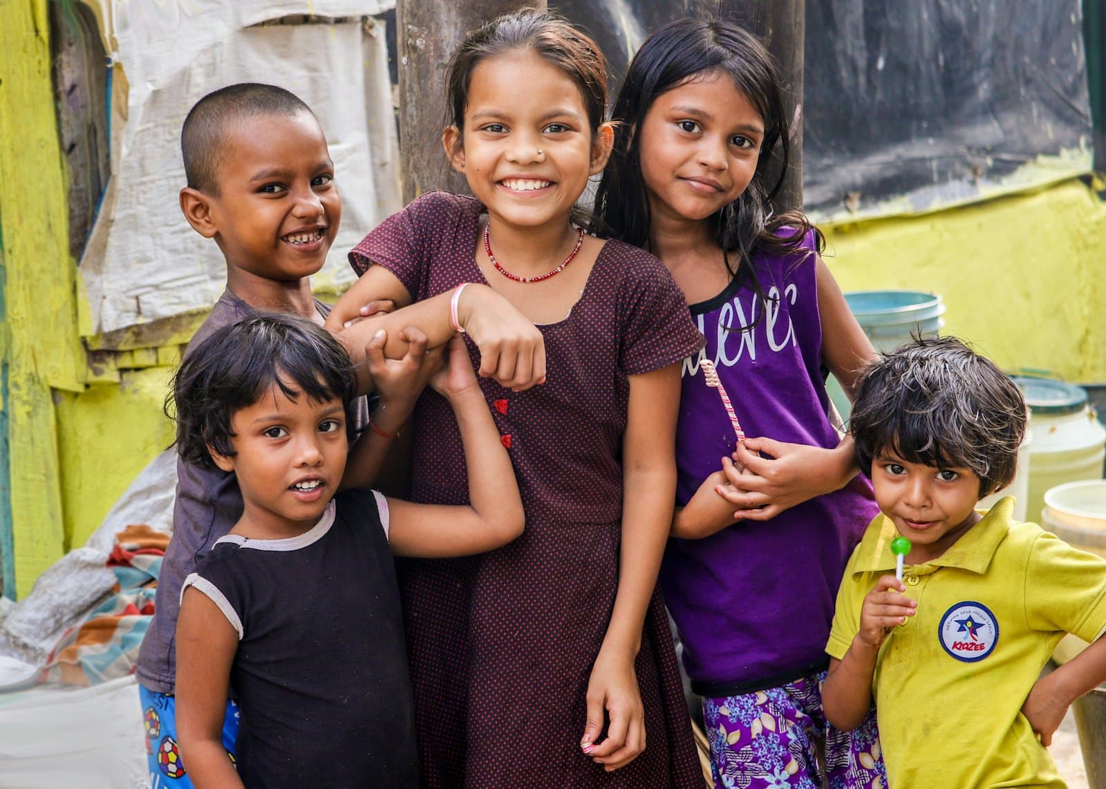 A group of children standing together and smiling outside a community building.